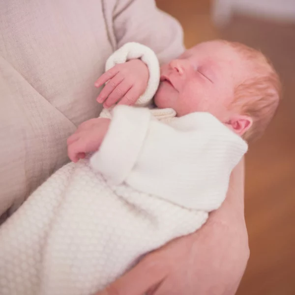 Baby wird von der Mutter getragen, das Baby trägt Jacke León Creme